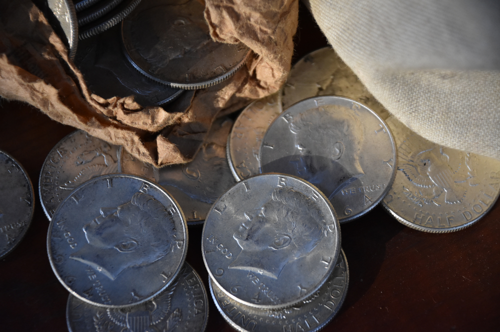 Vintage Kennedy half dollars spilling from a paper roll – sell silver coins to Coin Buyers in Lubbock.